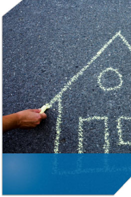 Man drawing a house on pavement with chalk.